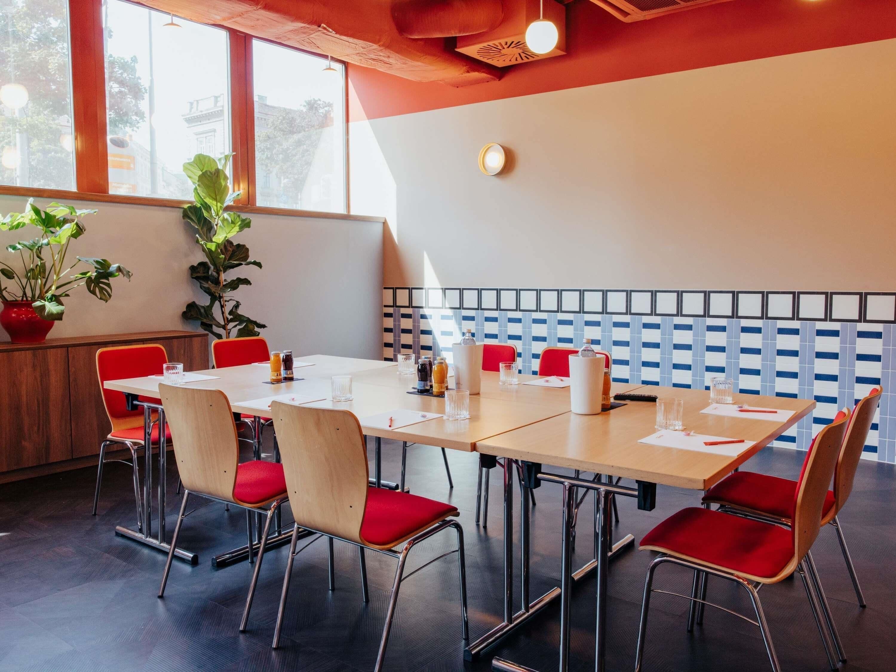 Une salle de conférence avec une longue table, des chaises rouges et des plantes en pot.