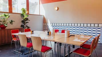 A conference room with a long table, red chairs, and potted plants.