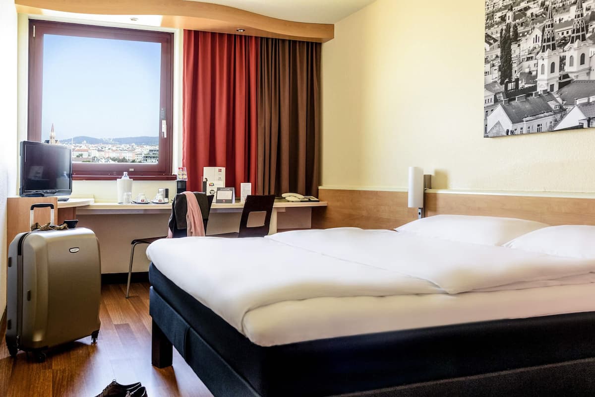 A hotel room with a bed, desk, chair, television, and a window with curtains.