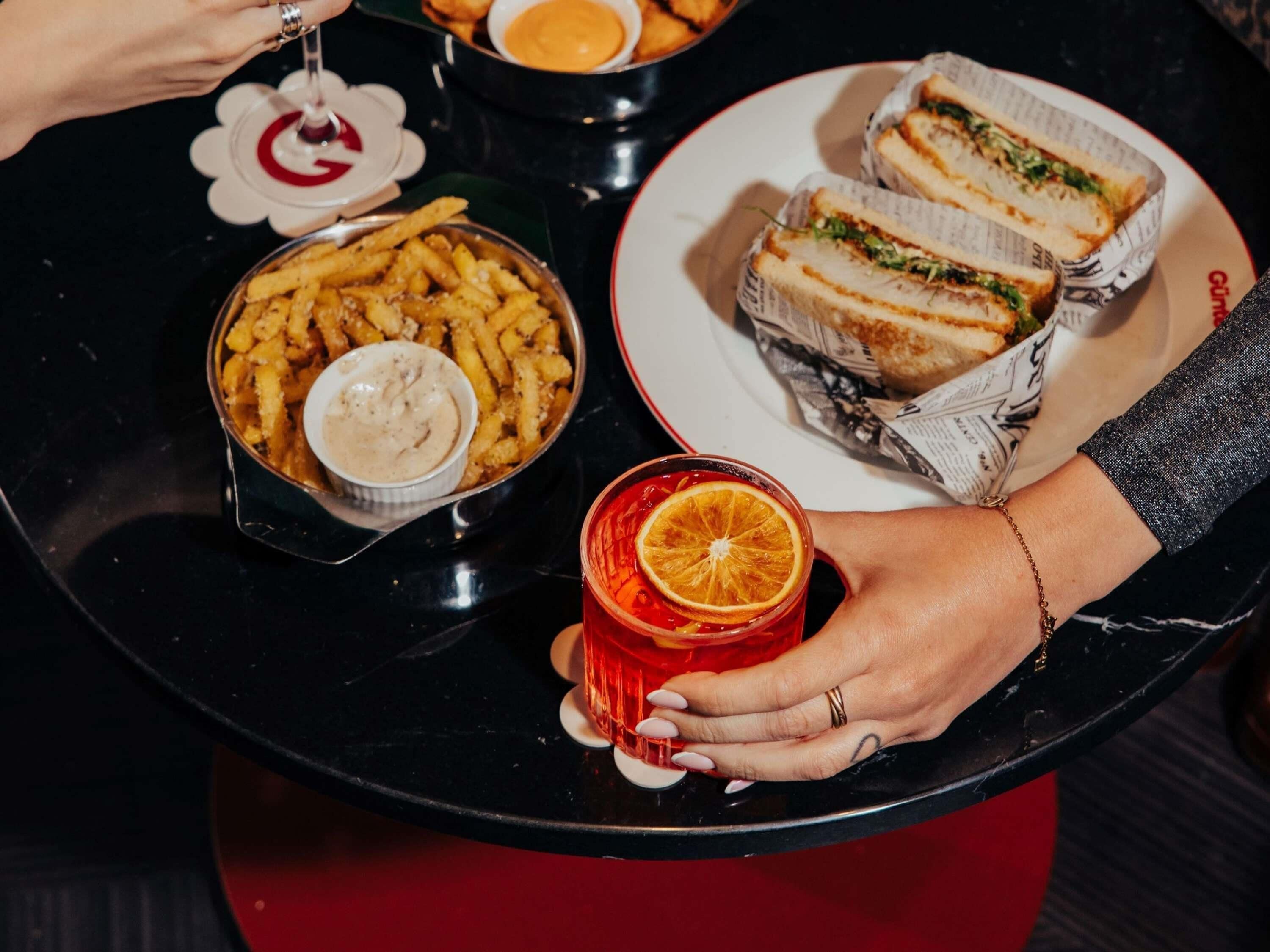 A tray with sandwiches, fries, and a drink, held by hands.