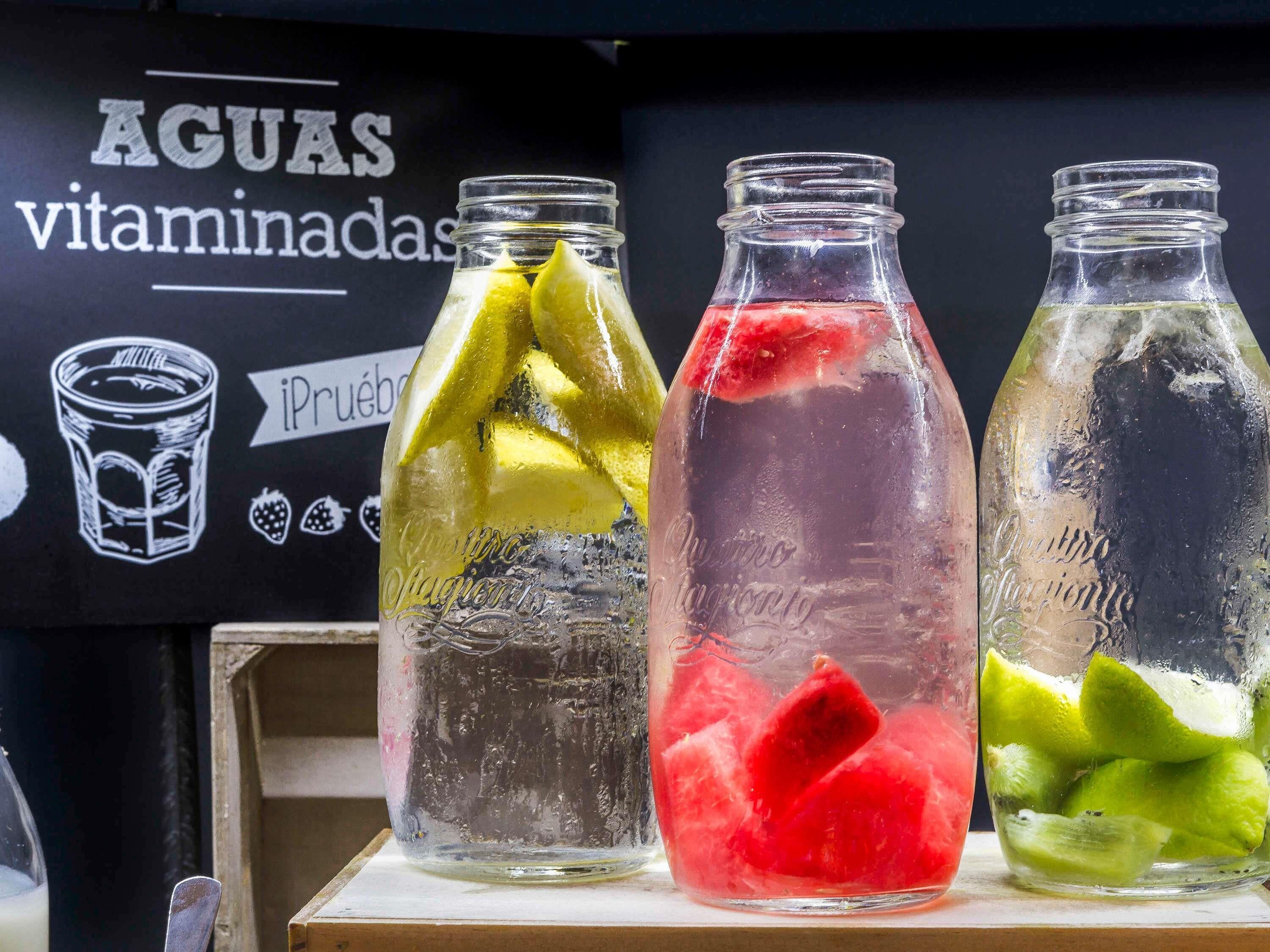 Drei Glasflaschen mit farbigen Flüssigkeiten und Fruchtstücken auf einer Holztischplatte.