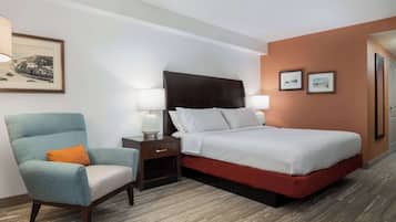 A hotel room with a bed, a nightstand, a chair, and a framed picture on the wall.