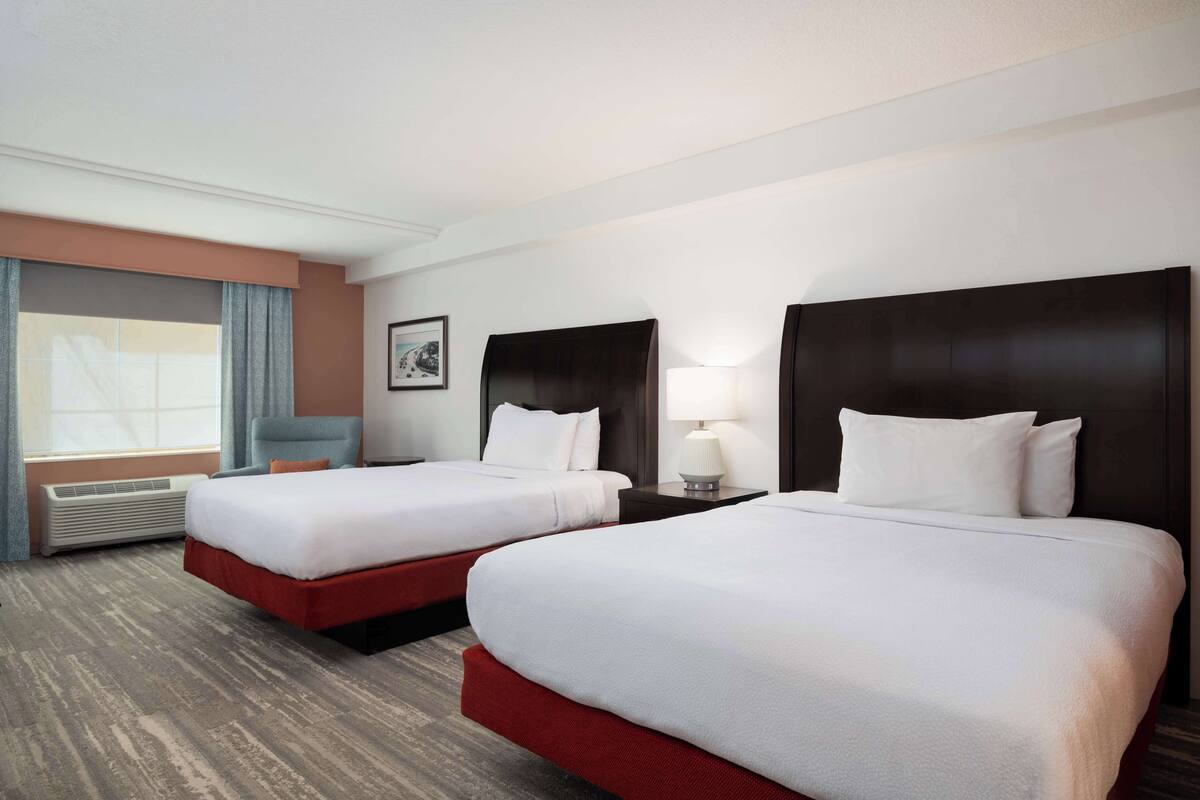Habitación de hotel con dos camas, una ventana con cortinas, una lámpara y un cuadro en la pared.
