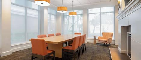A modern dining area with a large wooden table and orange chairs, large windows, and a fireplace.