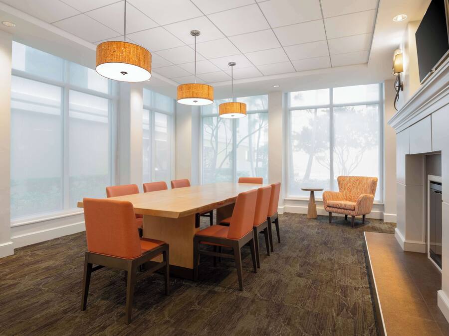 A modern dining area with a large wooden table and orange chairs, large windows, and a fireplace.