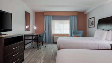 A hotel room with a bed, a desk with a chair, a TV, and a window with curtains.