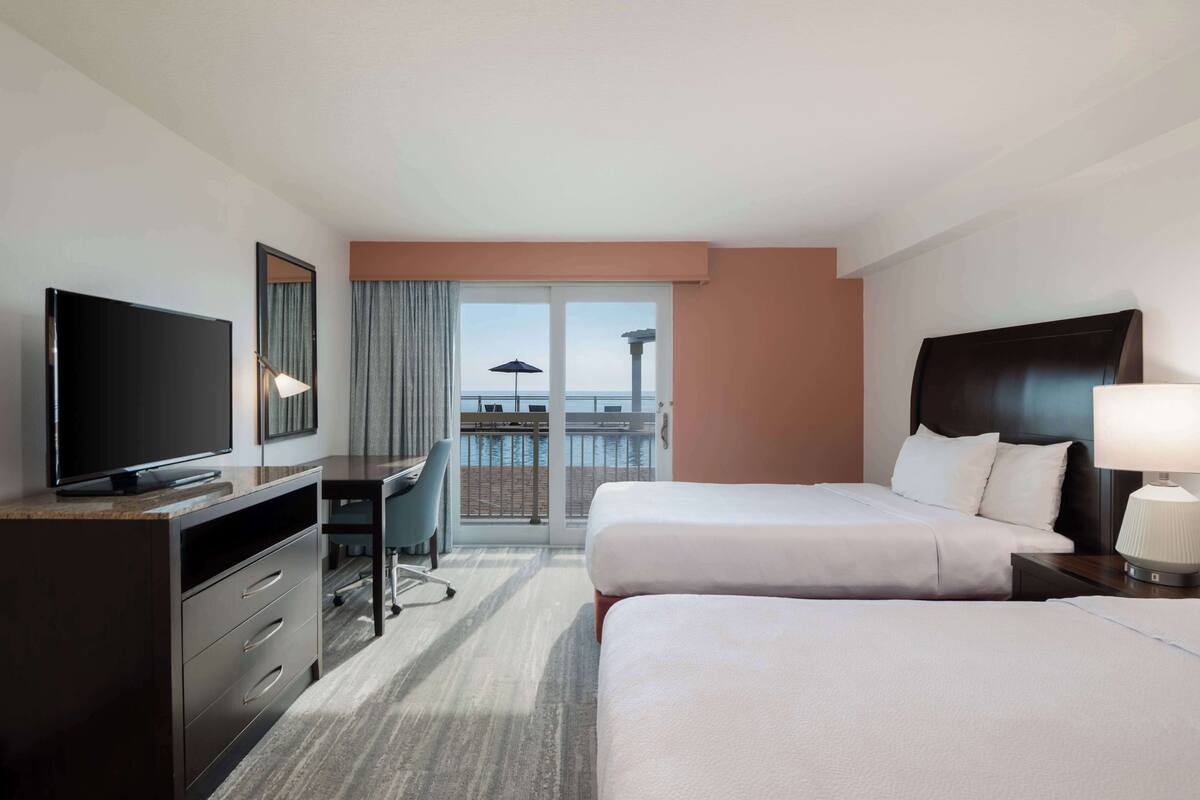 A hotel room with a bed, a desk, a television, and a view of the ocean.