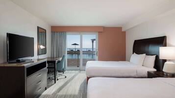 A hotel room with a bed, a desk, a television, and a view of the ocean.