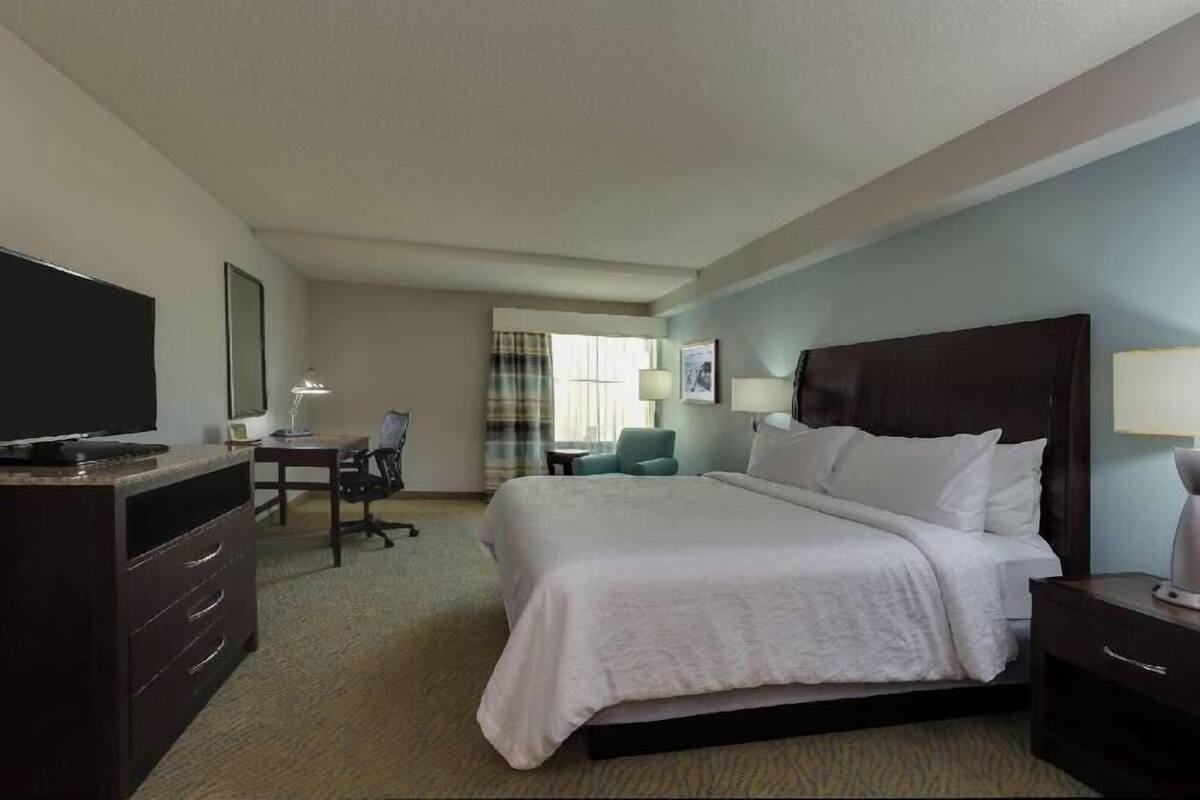 A hotel room with a bed, a desk, a chair, a television, and a window with curtains.
