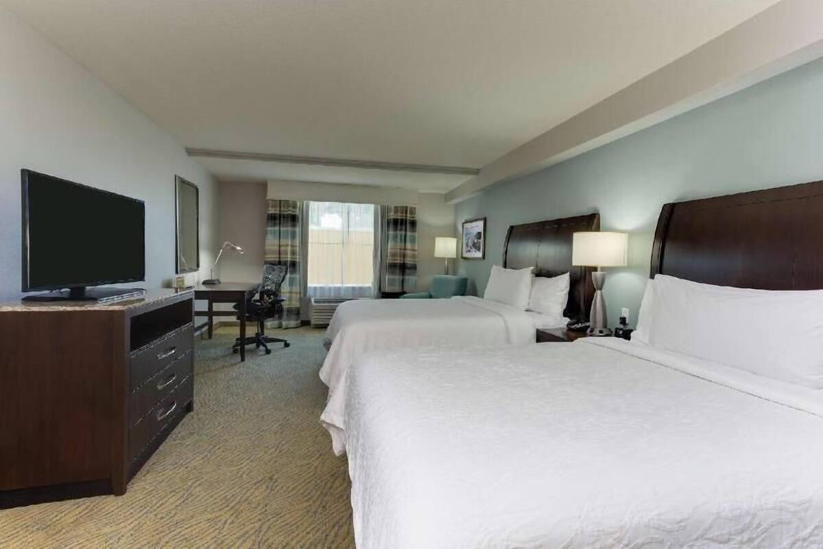 A hotel room with two beds, a desk, a television, and a window with curtains.