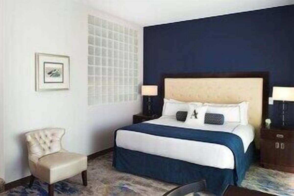 A hotel room with a bed, a chair, a nightstand, and a wall-mounted picture.