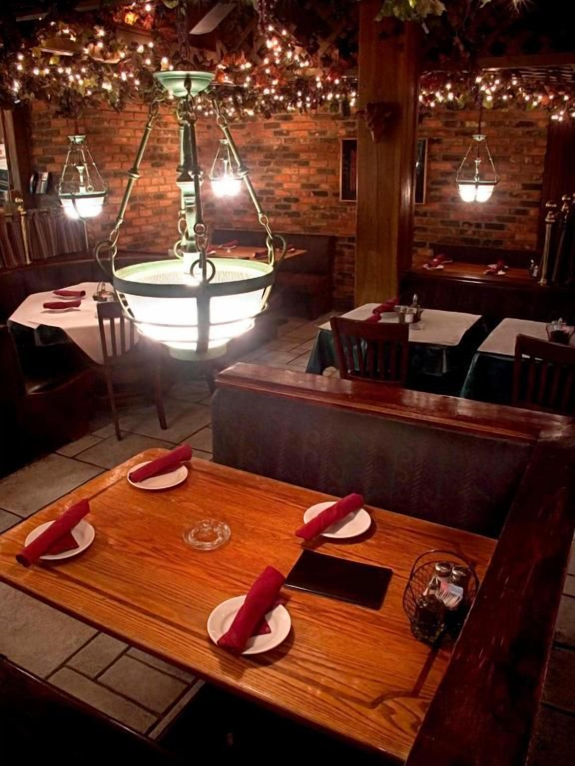 A restaurant with a wooden table set for four, a hanging light fixture, and brick walls.