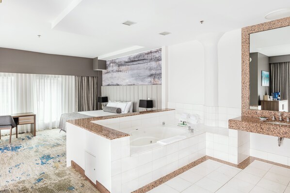 A modern hotel bathroom with a large bathtub, a separate shower area, and a vanity with a granite countertop.