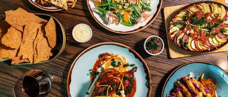 A variety of dishes on a wooden table, including grilled chicken, a vegetable tart, and a seafood dish.