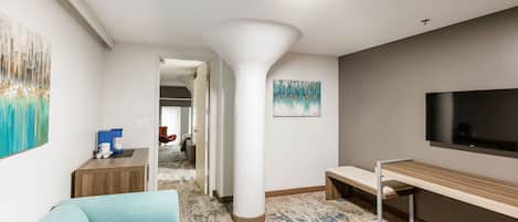 Habitación de hotel moderna con sofá, estación de café, televisor y un pilar grande.