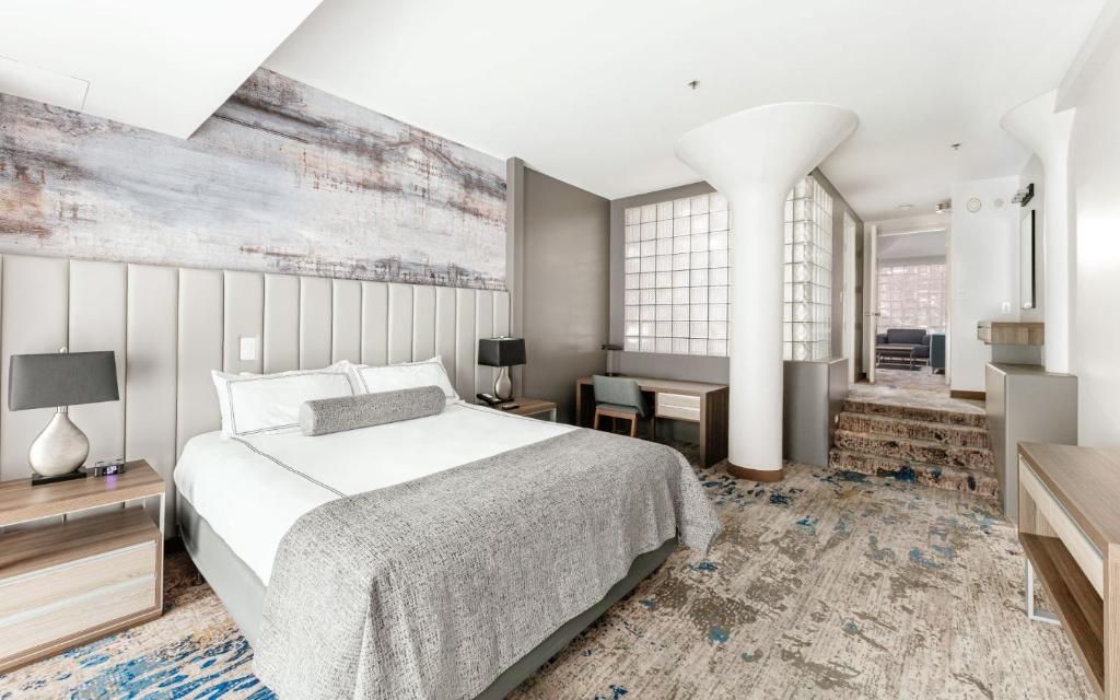 A modern hotel room with a large bed, a desk, and a view of the city.