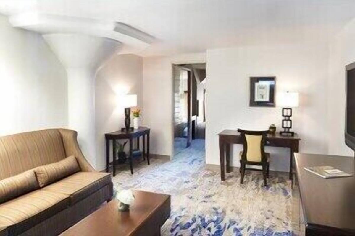 A hotel room with a sofa, a desk, a chair, a TV, and a lamp.