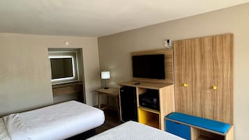 Ein Hotelzimmer mit zwei Betten, einem Fernseher, einem Schreibtisch und einem Kleiderschrank.