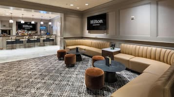 Een moderne lounge met een bar, zitplaatsen en een televisiescherm waarop 'Hilton Minneapolis' staat.
