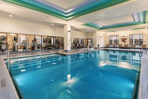 Una amplia piscina interior con agua cristalina, rodeada de tumbonas y equipo de ejercicio.