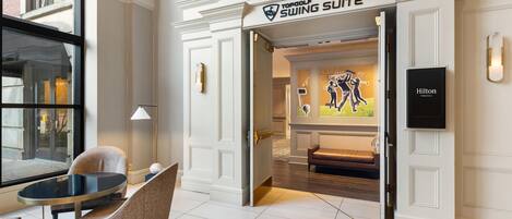 Vestíbulo de hotel con un letrero que dice 'Swing Suite', un área de descanso con mesa y sillas, y vista al interior a través de una puerta abierta.