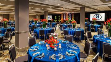 A banquet hall with round tables set for dining, featuring blue tablecloths and silverware.