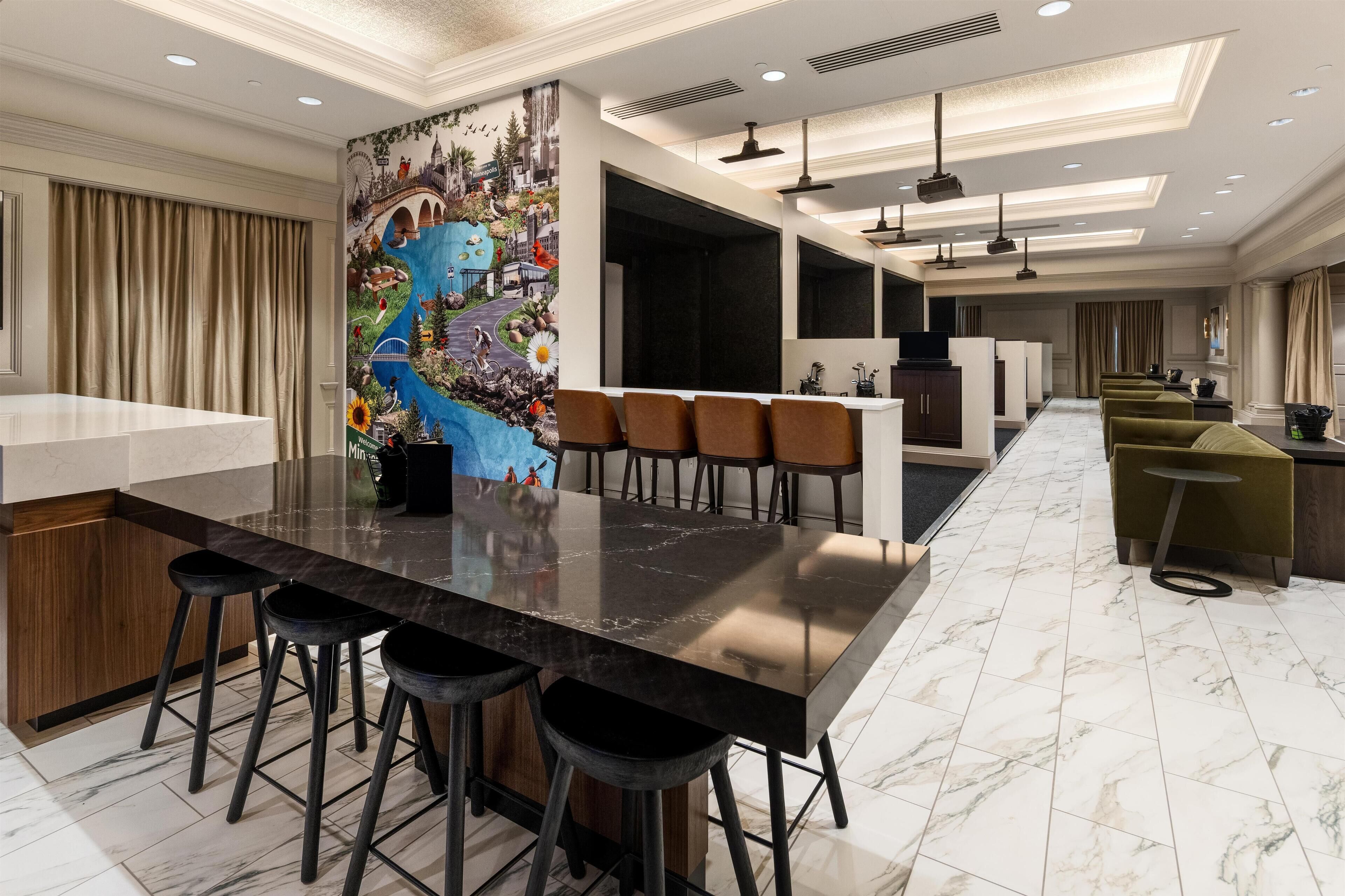 A modern hotel lobby with a long bar area, a mural on the wall, and a seating area with chairs and stools.