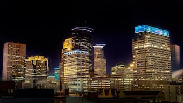 A nighttime cityscape with illuminated skyscrapers, including a prominent building with a unique top structure and another with a blue-lit top.