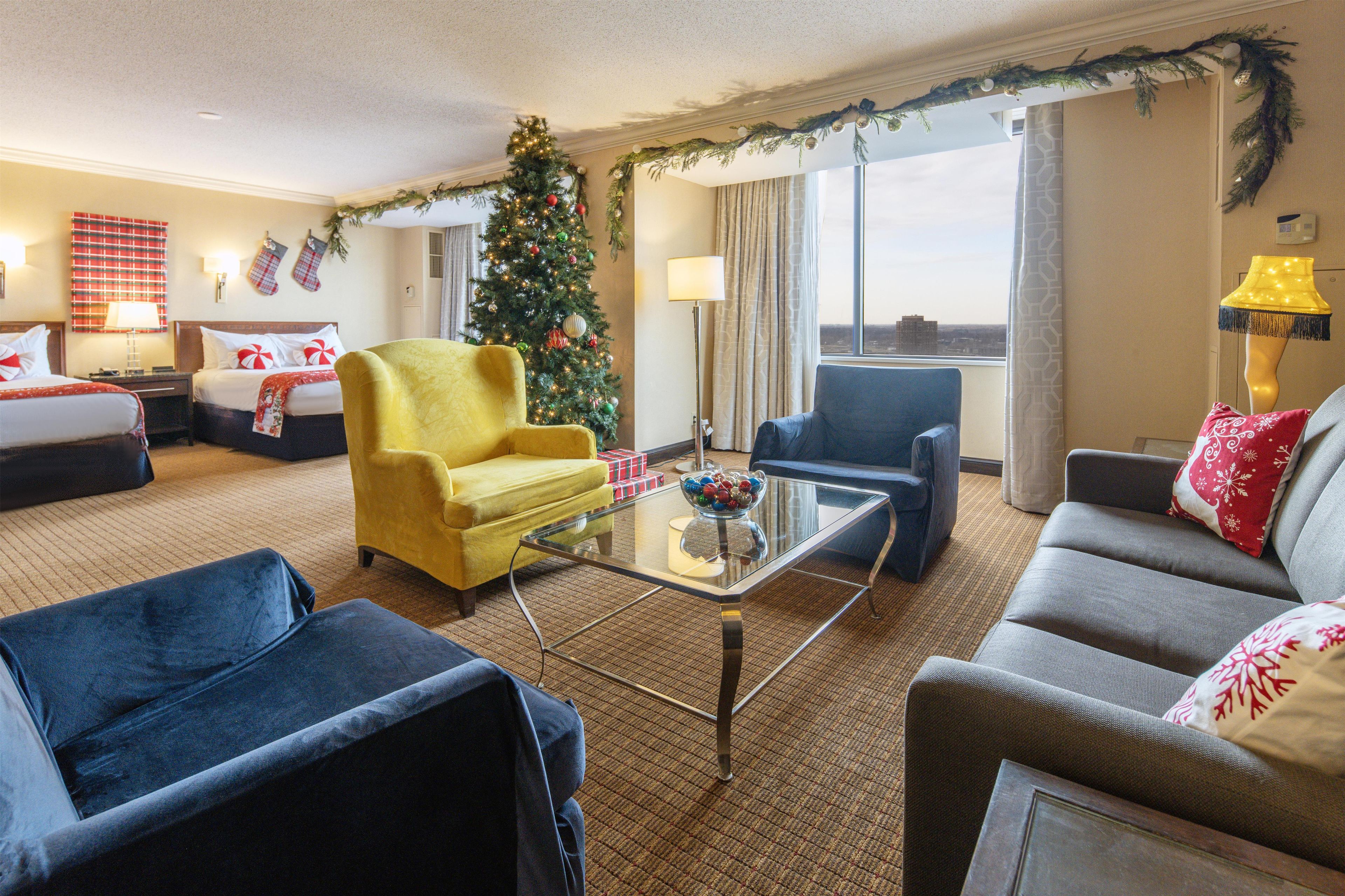 A hotel room with two beds, a Christmas tree, a glass coffee table, and a view of the city.