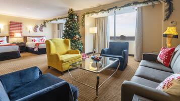 A hotel room with two beds, a Christmas tree, a glass coffee table, and a view of the city.