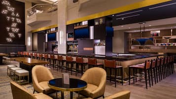 Zona bar moderna con diverse opzioni di seduta, tra cui sgabelli da bar e tavoli rotondi, e un bancone bar con una vasta selezione di bottiglie.