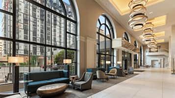 A spacious lobby with large windows, modern furniture, and a high ceiling with circular light fixtures.