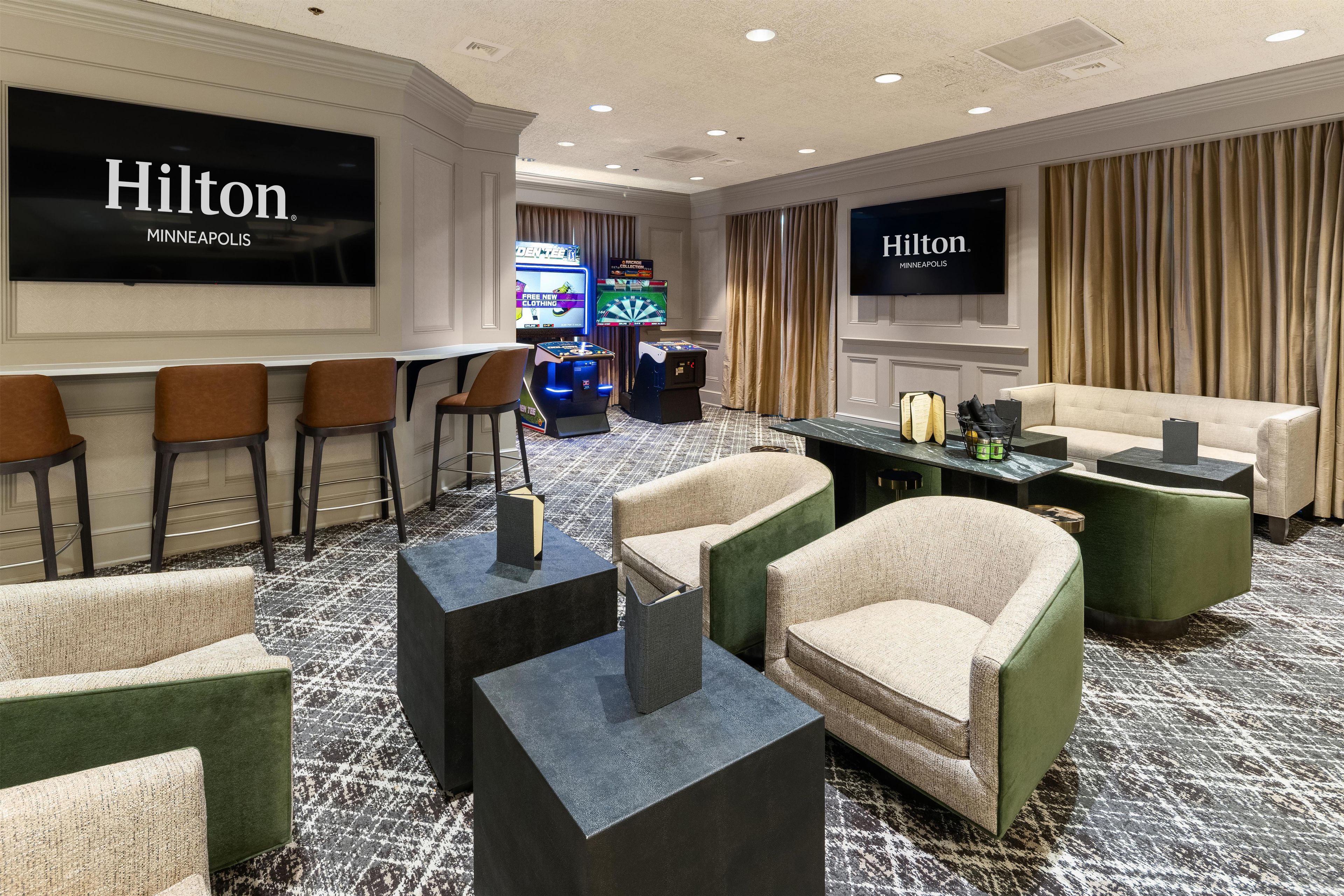 A hotel lobby with seating, a bar area, and a television screen displaying the hotel's name.