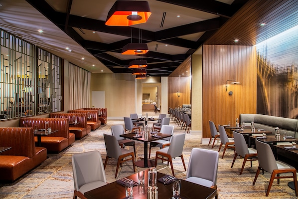 Un vestíbulo de hotel con sillones de cuero, mesas de comedor y una gran pared de madera.