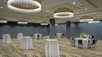 Een ruime balzaal met ronde tafels, witte tafellakens en elegante kroonluchters.