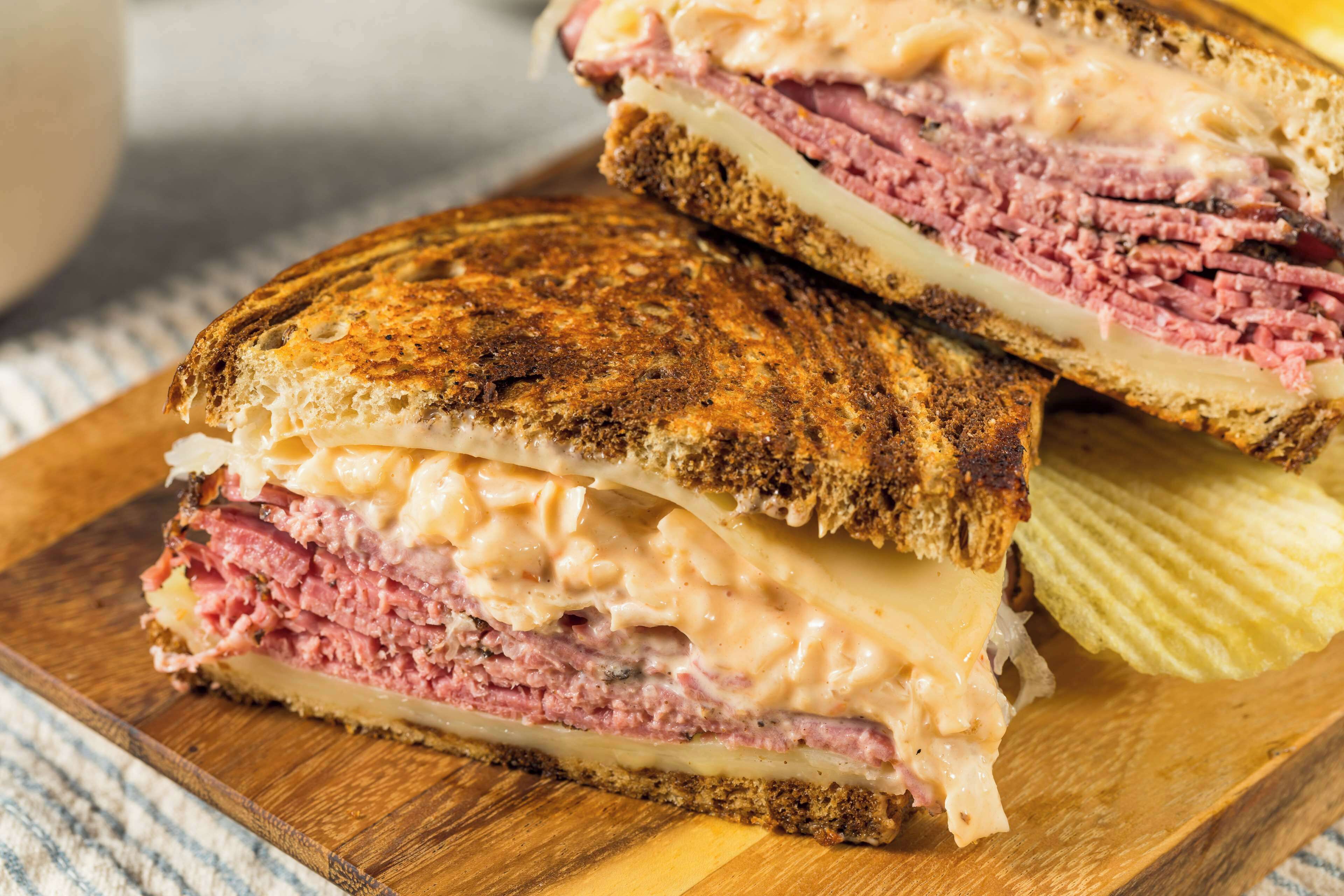 A grilled sandwich with layers of meat and cheese on a wooden board.