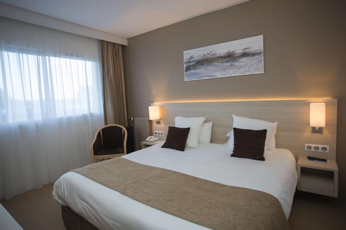 Habitación de hotel con una cama grande, dos lámparas de noche, una mesita de noche con teléfono y una silla.