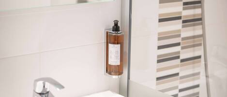A modern bathroom with a glass shower enclosure, a white sink, and a bottle of hand soap on the wall.