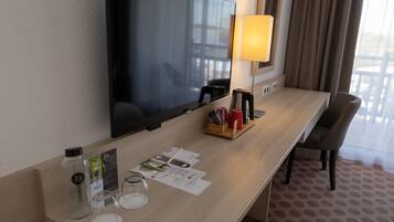 Une chambre d’hôtel équipée d’un téléviseur à écran plat fixé au mur, d’une table de chevet avec une lampe, d’une machine à café et d’une chaise.