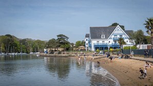 A beach with a large building, a calm lake, and boats in the background. - Best Western Plus Hôtel Le Roof (Vannes)