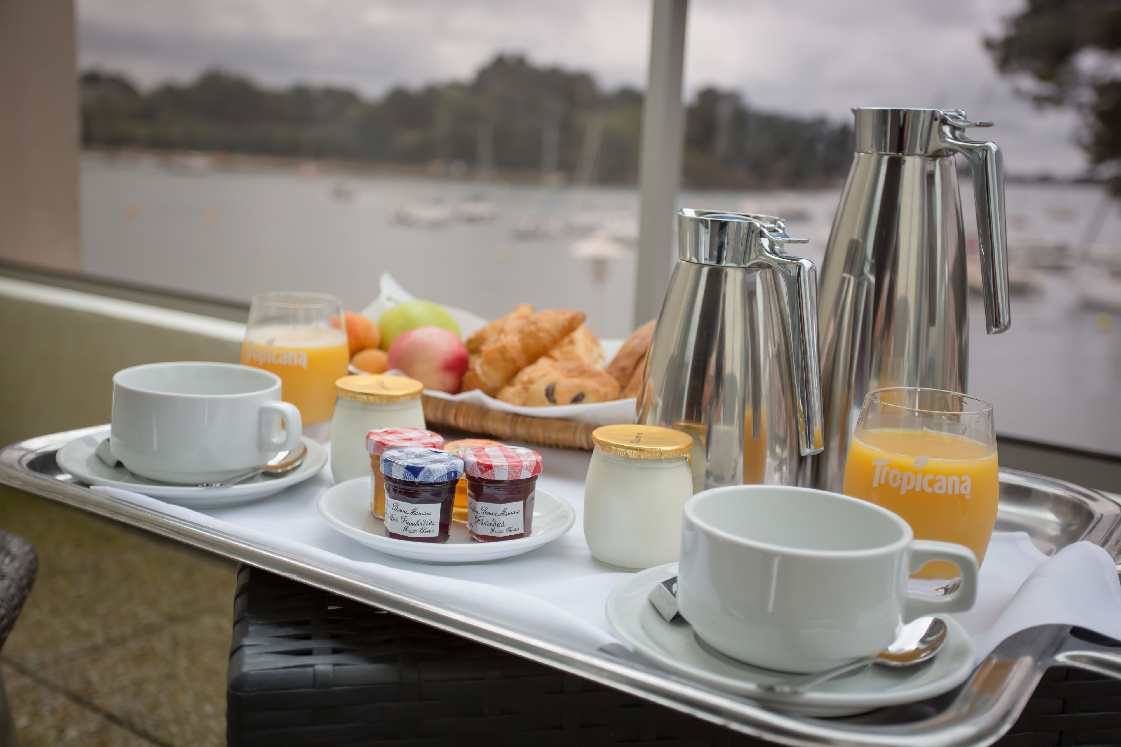 Bandeja de desayuno con cruasanes, fruta, jugo y café en un balcón con vista a un lago.