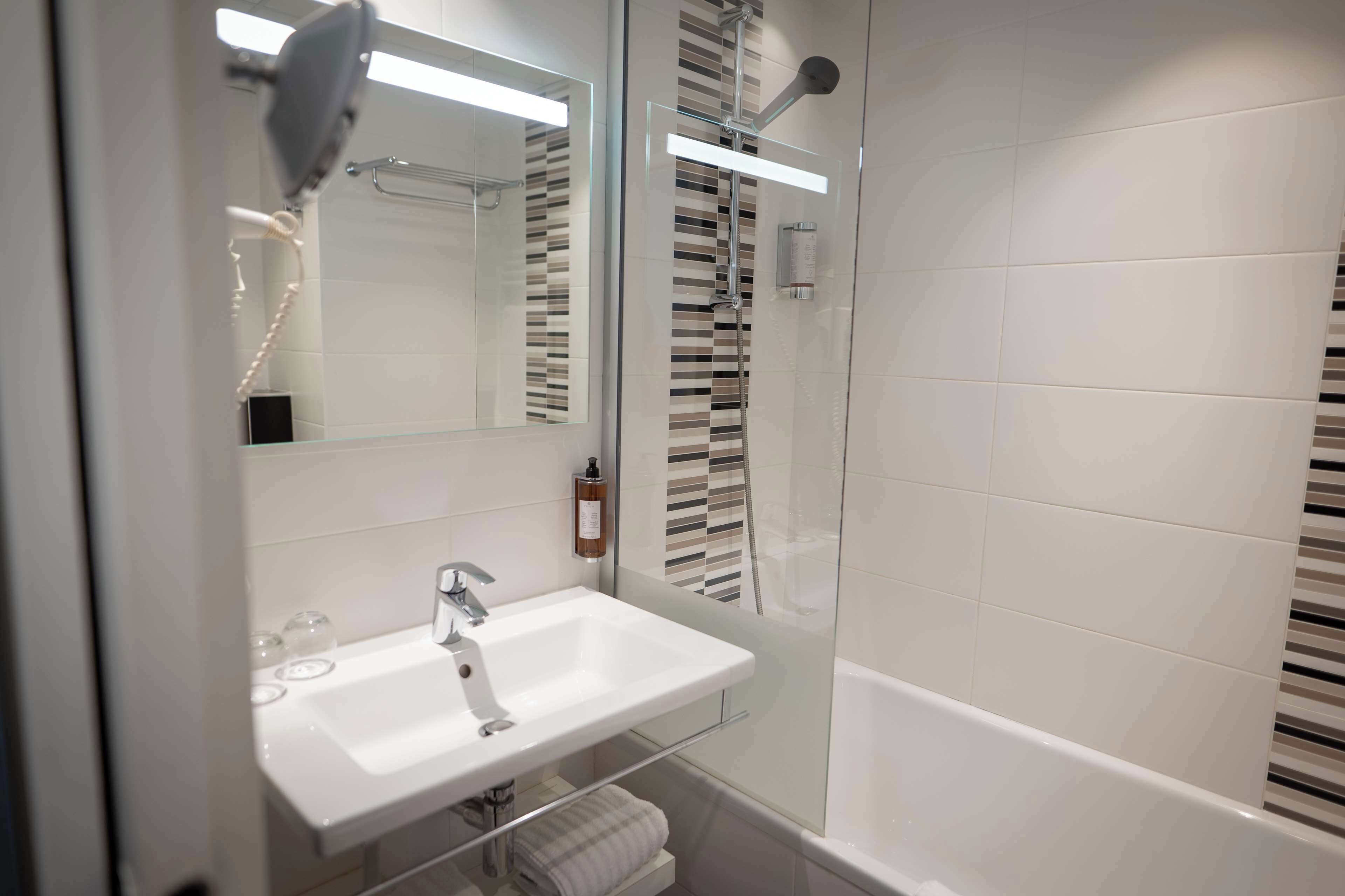 Un baño moderno con lavamanos, espejo y ducha blancos.