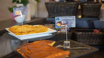 A buffet table with a variety of food items, including a large piece of cake and a plate of what appears to be a casserole or casserole-like dish. There are also baskets in the background, possibly containing additional food items.