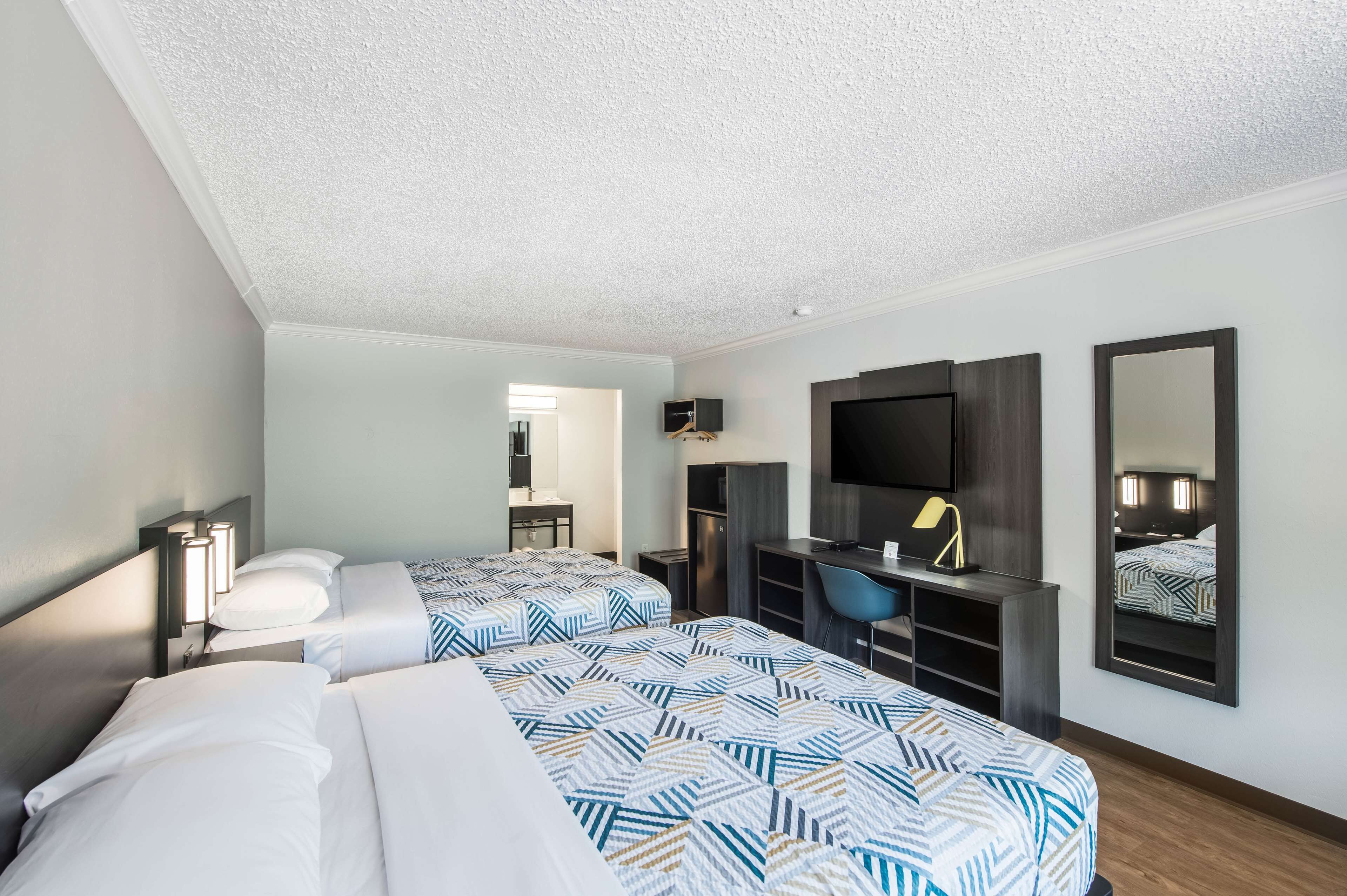 A hotel room with two beds, a desk, a chair, a TV, and a mirror.
