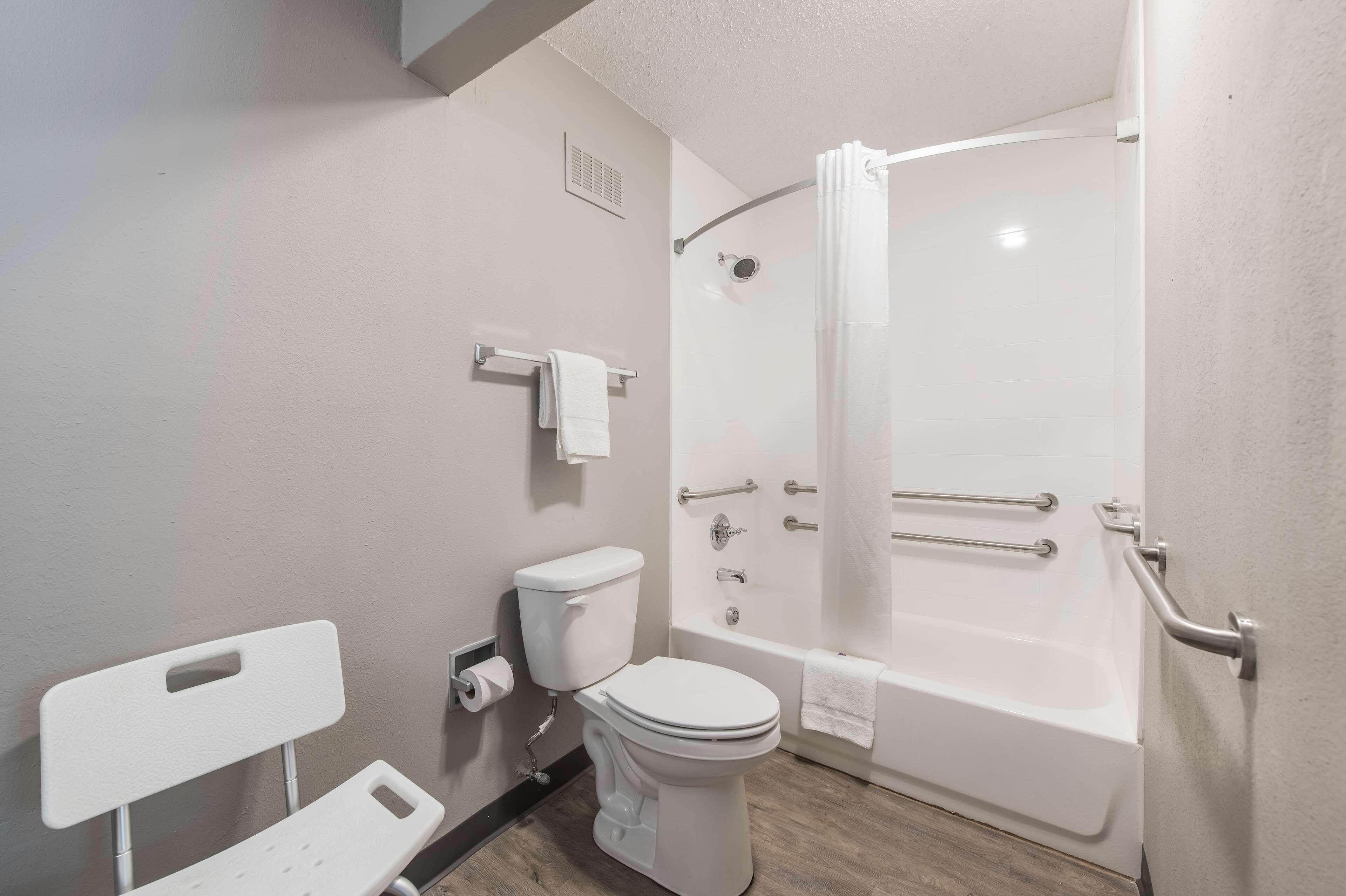 A bathroom with a toilet, a shower with grab bars, and a white sink.
