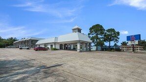 A motel with a large parking lot, a covered outdoor area, and a sign indicating the name and room types. - Motel 6 Kilgore, TX (Kilgore)