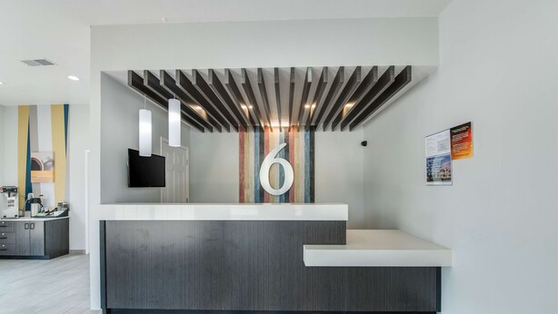 A reception desk with a large '6' sign, a modern design with a slatted ceiling, and a colorful striped rug. - Motel 6 Kilgore, TX (Kilgore)