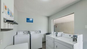A laundry area with two Whirlpool washers and dryers, a mirror, and a sign indicating a motorized response system. - Motel 6 Kilgore, TX (Kilgore)