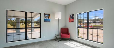 A spacious room with large windows, a red chair, and a floor lamp.