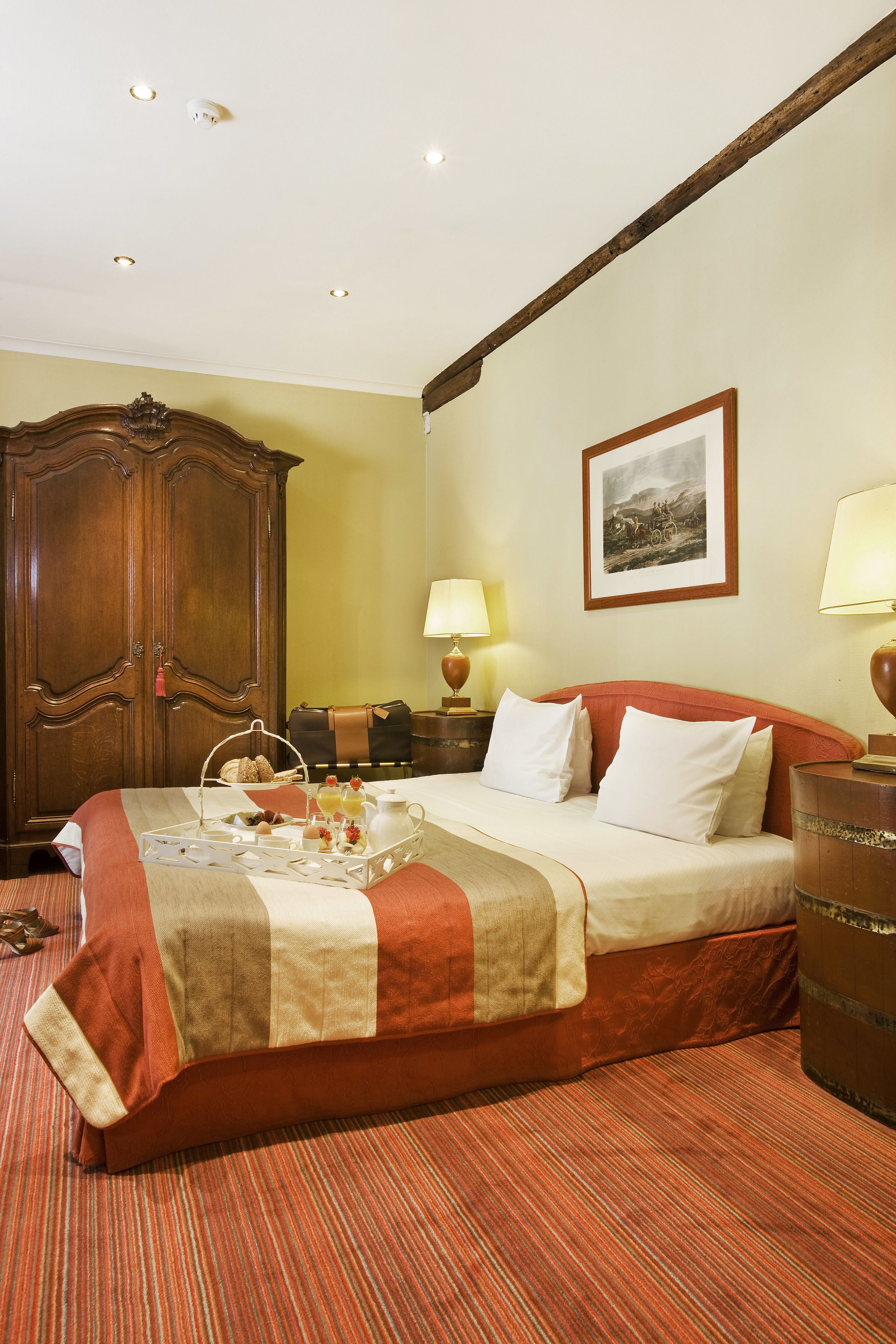 A hotel room with a large bed, a wooden wardrobe, a framed picture on the wall, and two bedside lamps.